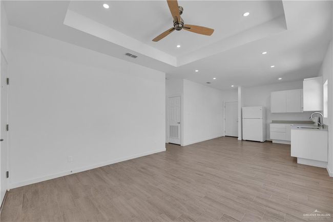 Unfurnished living room featuring a raised ceiling, ceiling fan, sink, and light hardwood / wood-style floors | Image 7