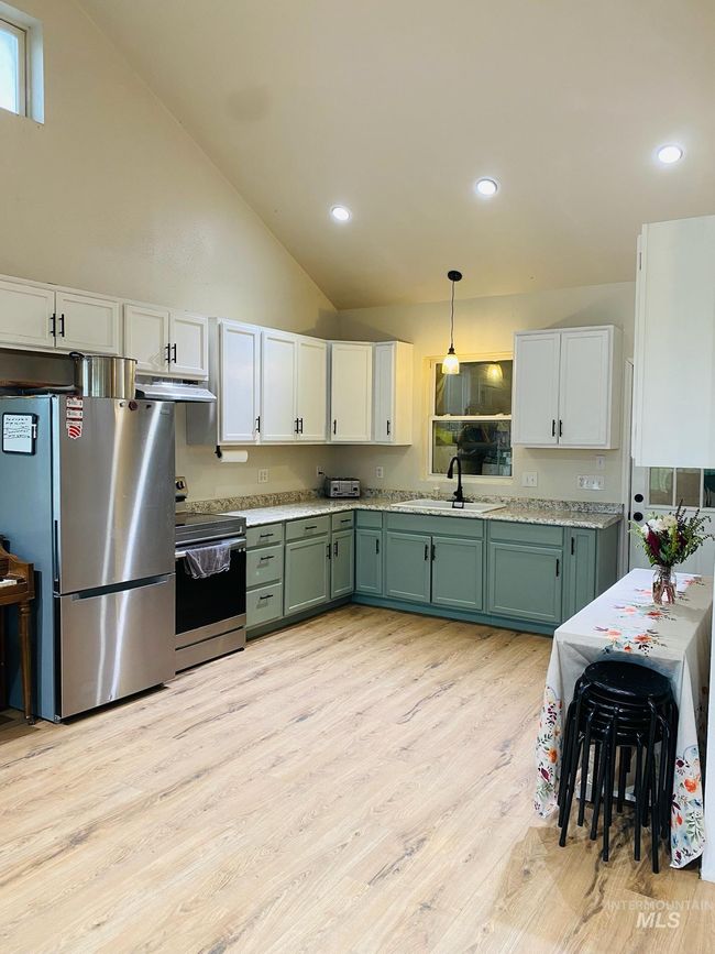 Kitchen featuring stainless steel appliances, under cabinet range hood, green cabinets, light wood finished floors, and light countertops | Image 13