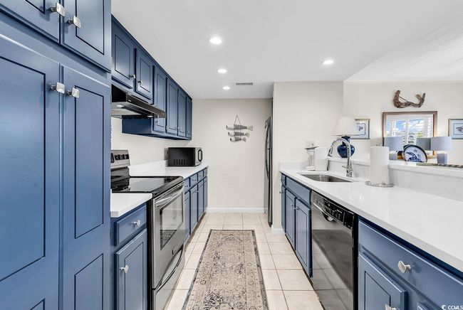 Kitchen featuring a sink, light countertops, under cabinet range hood, visible vents, and black appliances | Image 7