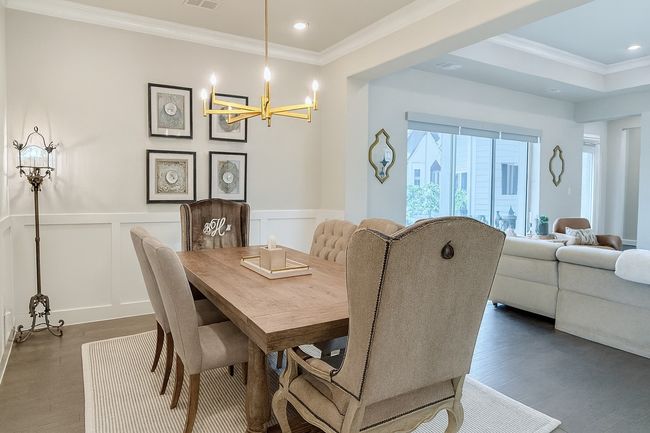 Dining space featuring crown molding, a chandelier, a decorative wall, wood finished floors, and a wainscoted wall | Image 4