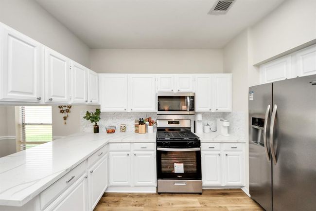 This bright, open kitchen features abundant cabinet storage and generous quartz countertops, providing plenty of room for cooking and gathering. With its open layout, it flows seamlessly into the adjacent living spaces—never feeling closed off, but inviting and connected. | Image 20