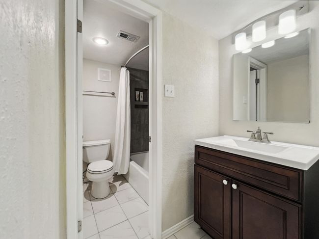 Bathroom featuring shower / bath combo, vanity, a textured wall, and light tile patterned floors | Image 10