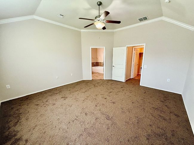 Unfurnished bedroom with vaulted ceiling, carpet floors, ensuite bath, ornamental molding, and ceiling fan | Image 9