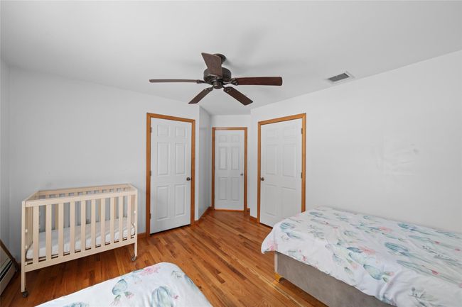 Bedroom with wood finished floors, visible vents, baseboards, baseboard heating, and ceiling fan | Image 32