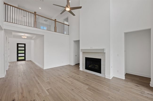 Unfurnished living room featuring a high ceiling, a ceiling fan, wood finished floors, a tile fireplace, and baseboards | Image 5