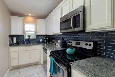 Kitchen with stainless steel appliances, sink, tasteful backsplash, light stone countertops, and white cabinets - 2215 | Image 2