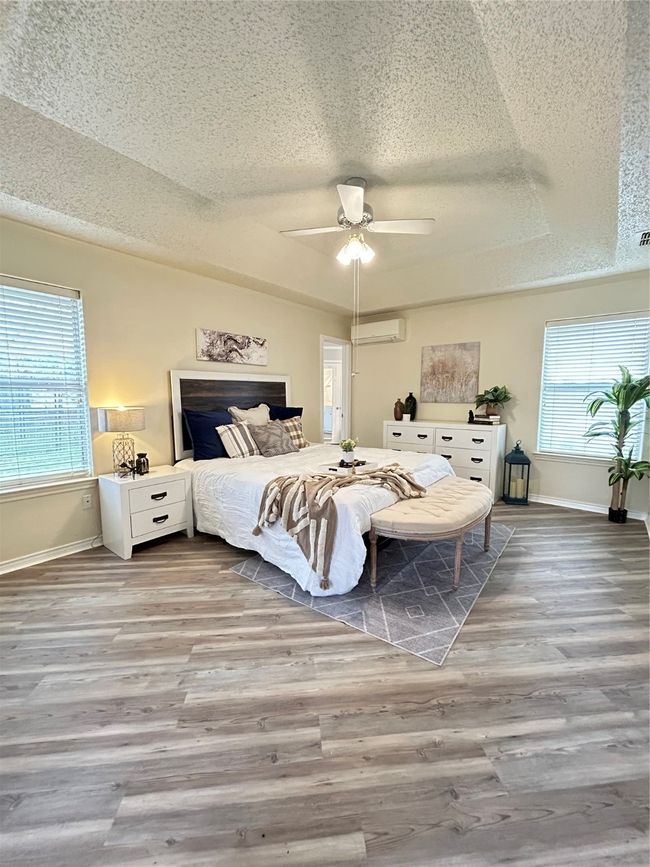 Bedroom featuring baseboards, a wall mounted air conditioner, a tray ceiling, wood finished floors, and a textured ceiling | Image 32