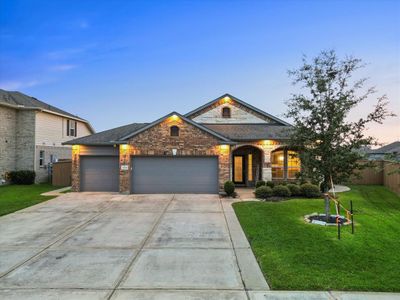 Charming single-story home with a well-maintained brick facade, featuring a three-car garage, neat landscaping, and a welcoming entryway, captured at dusk with exterior lights adding a cozy glow. | Image 1