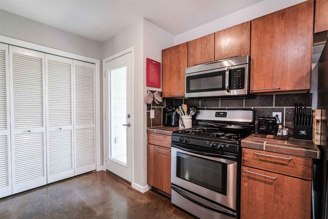 Kitchen with brown cabinets, dark countertops, stainless steel appliances, finished concrete floors, and backsplash | Image 7