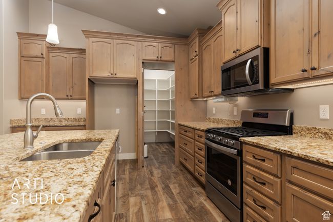 Kitchen with appliances with stainless steel finishes, dark wood-style floors, light stone counters, decorative light fixtures, and vaulted ceiling | Image 17