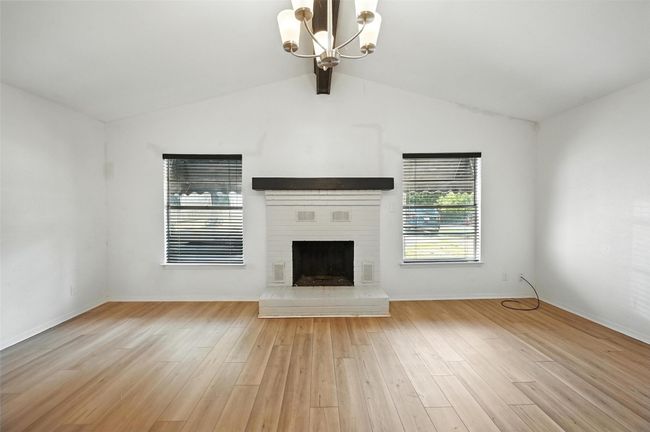 Unfurnished living room featuring a chandelier, light wood-type flooring, and a brick fireplace | Image 8