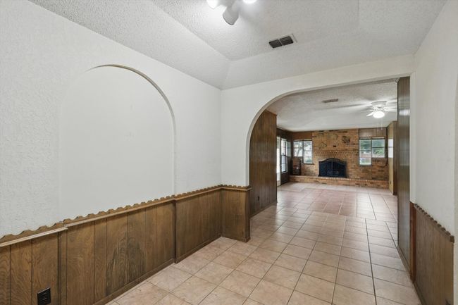 Hallway with a textured ceiling, wood walls, a wainscoted wall, arched walkways, and light tile patterned floors | Image 12