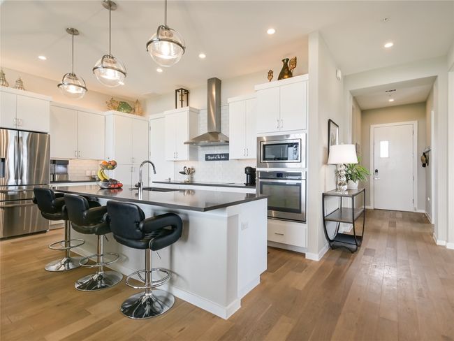 This kitchen features under/above cabinet lighting, huge entertaining island, upgraded pendant lights, roll-out pantry shelves, upgraded Bosch induction cooktop, stainless appliances, and tons of storage cabinetry space. | Image 6