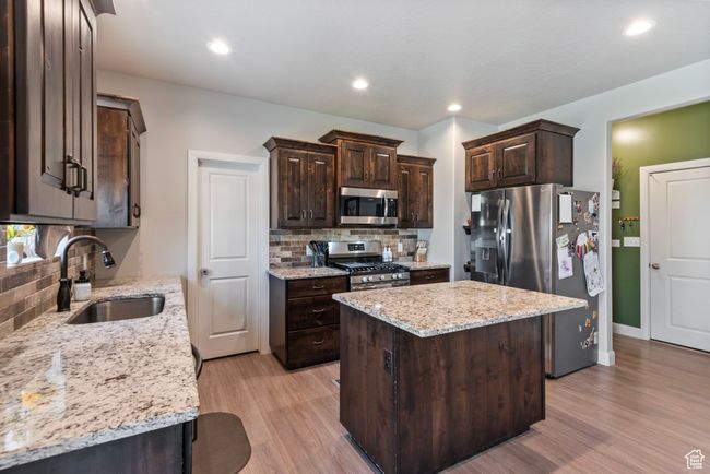 Kitchen featuring light wood-style flooring, dark brown cabinetry, stainless steel appliances, a kitchen island, and a sink | Image 4