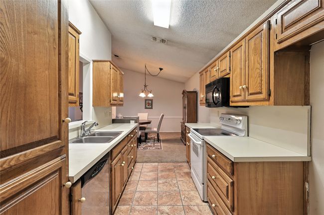 Kitchen with electric range, a textured ceiling, dishwasher, light countertops, and black microwave | Image 15