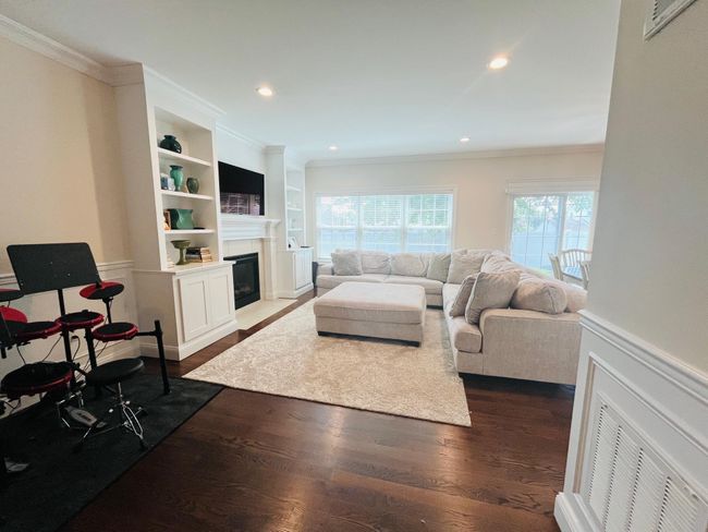 Living room featuring a chandelier, crown molding, dark wood-type flooring, a wainscoted wall, and stairway | Image 4