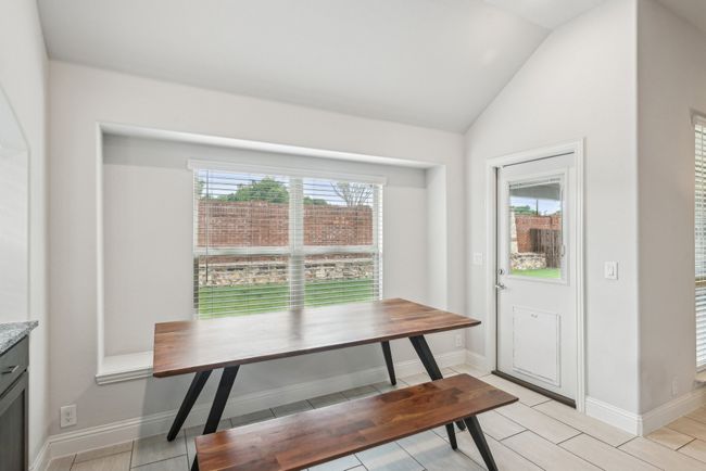 Bench seating in breakfast with view of backyard and kitchen/living area, featuring healthy amount of natural light, vaulted ceiling, and tile flooring | Image 16