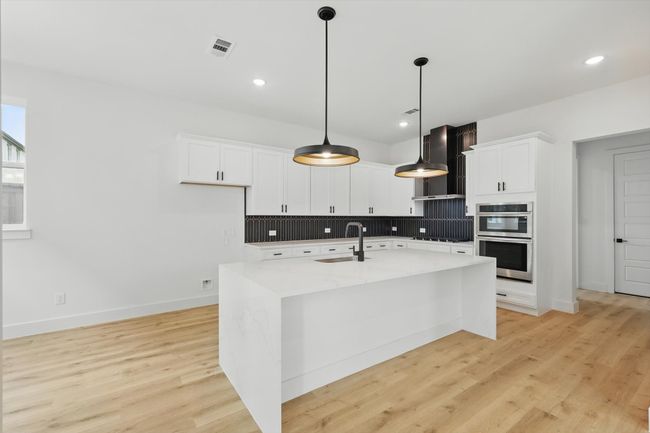 Kitchen featuring stainless steel double oven, wall chimney exhaust hood, a sink, decorative backsplash, and stovetop | Image 18