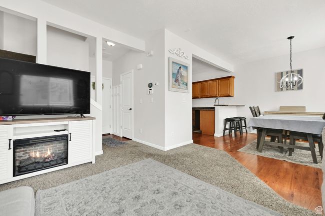 Living area featuring a warm lit fireplace, baseboards, an inviting chandelier, and wood finished floors | Image 28