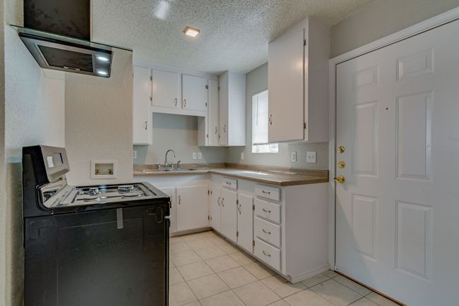 Kitchen featuring light tile patterned floors, black gas range oven, white cabinetry, and a textured ceiling | Image 9