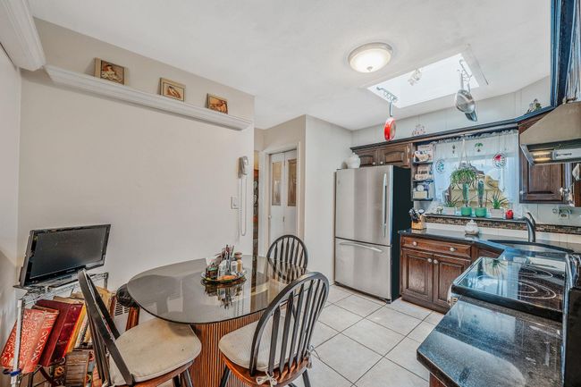 Kitchen with freestanding refrigerator, a skylight, dark countertops, light tile patterned floors, and electric range oven | Image 9