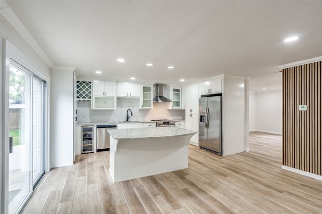 Kitchen featuring stainless steel appliances, wall chimney exhaust hood, wine cooler, a kitchen island, and crown molding | Image 12