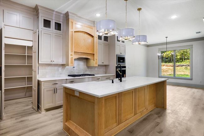 Kitchen with tasteful backsplash, glass insert cabinets, light wood-type flooring, a chandelier, and ornamental molding | Image 12