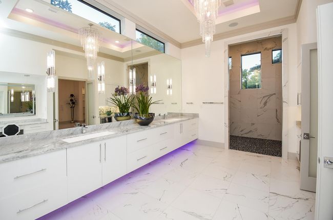 This luxurious bathroom features a spacious double vanity with elegant Carrarra white marble countertops, modern lighting fixtures and ambient lighting, and a large walk-in shower. The high ceilings and large windows provide ample natural light, creating a bright and inviting atmosphere. | Image 25
