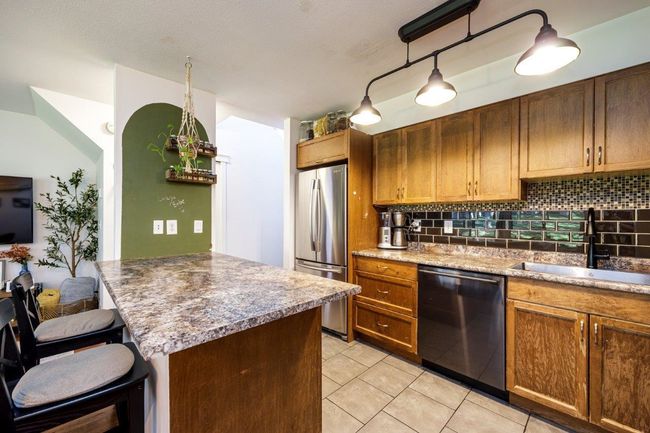Kitchen with light tile patterned floors, a breakfast bar, a sink, decorative backsplash, and appliances with stainless steel finishes | Image 5