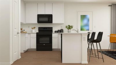 Kitchen with a kitchen bar, black appliances, white cabinetry, and light hardwood / wood-style flooring | Image 2