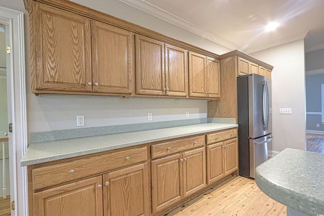Kitchen with freestanding refrigerator, light wood finished floors, crown molding, and brown cabinets | Image 6