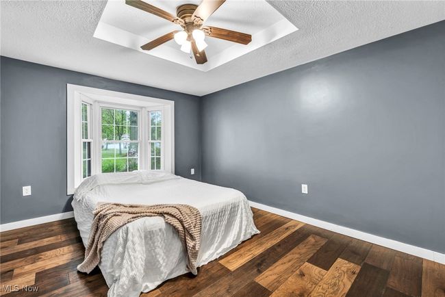 Bedroom featuring a baseboard heating unit, wood floors, ceiling fan, and a textured ceiling | Image 22