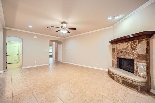 Unfurnished living room with a ceiling fan, arched walkways, a fireplace, ornamental molding, and recessed lighting | Image 7