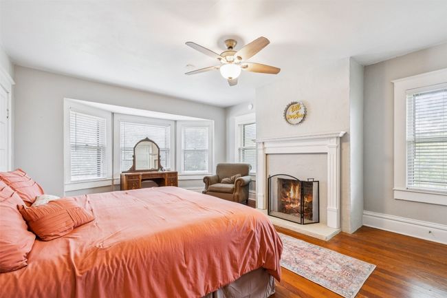 Bedroom featuring wood finished floors, a high end fireplace, and a ceiling fan | Image 28