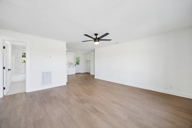 Unfurnished living room featuring a ceiling fan, plenty of natural light, wood finished floors, and crown molding | Image 4