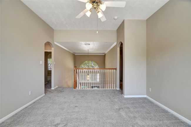 This spacious room features neutral walls and carpet, a ceiling fan, and an open railing with an arched window, offering a bright and airy feel. Perfect for a family area or office space. | Image 30