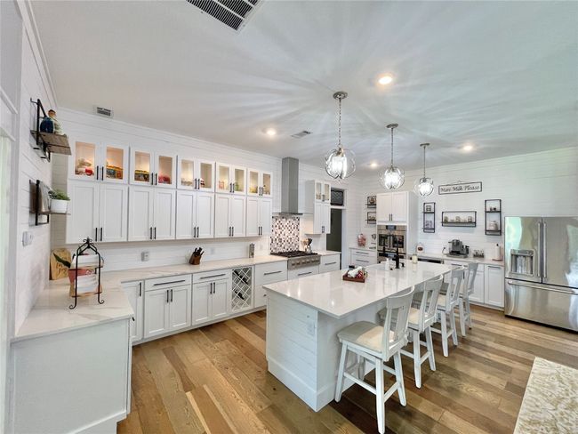 Kitchen with stainless steel appliances, wall chimney exhaust hood, tasteful backsplash, light countertops, and white cabinets | Image 13