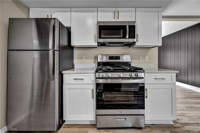 Kitchen featuring stainless steel appliances, light wood-style floors, white cabinets, light countertops, and wood walls | Image 8
