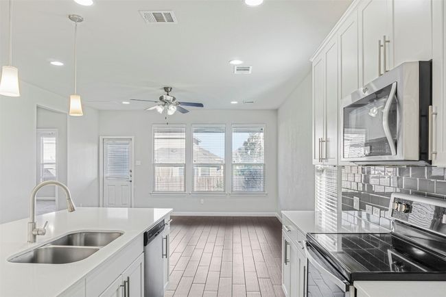 Kitchen featuring appliances with stainless steel finishes, ceiling fan, light wood-style flooring, backsplash, and light countertops | Image 13
