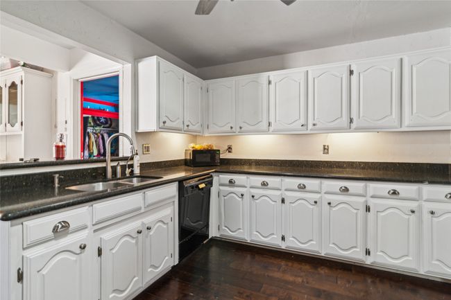 Kitchen with black appliances, dark countertops, white cabinetry, dark wood-type flooring, and ceiling fan | Image 6