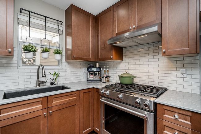 Kitchen featuring tasteful backsplash, a sink, under cabinet range hood, light stone countertops, and stainless steel gas range oven | Image 6