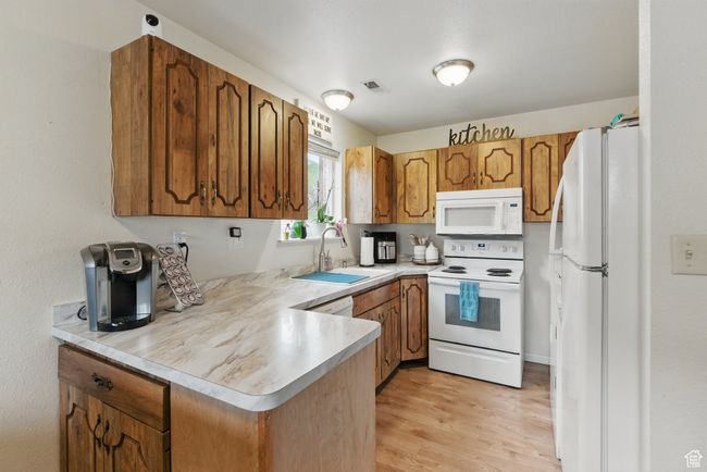 Kitchen featuring brown cabinets, light countertops, a sink, white appliances, and a peninsula | Image 26