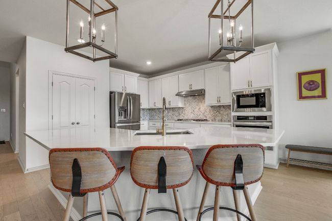 Kitchen featuring appliances with stainless steel finishes, backsplash, a chandelier, under cabinet range hood, and light wood finished floors | Image 10