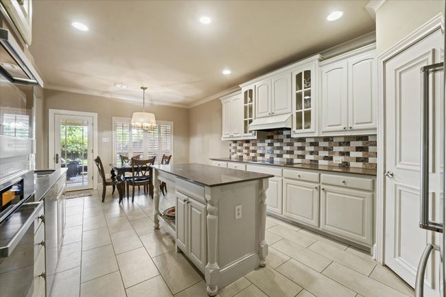 Kitchen with dark countertops, decorative backsplash, under cabinet range hood, black electric cooktop, and glass insert cabinets | Image 17