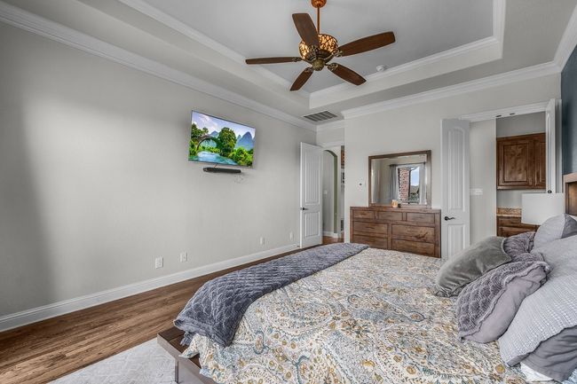 Bedroom with wood finished floors, a raised ceiling, baseboards, crown molding, and ceiling fan | Image 14