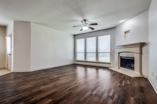 Unfurnished living room featuring a ceiling fan, wood finished floors, and a fireplace with raised hearth | Image 9