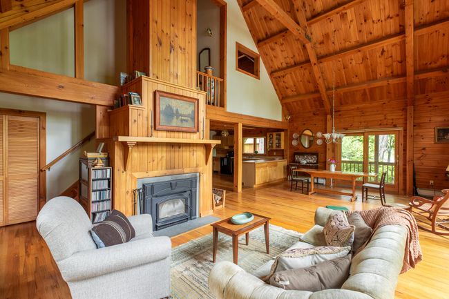 Living area featuring a fireplace with flush hearth, high vaulted ceiling, wood finished floors, a chandelier, and wooden ceiling with exposed beams | Image 7