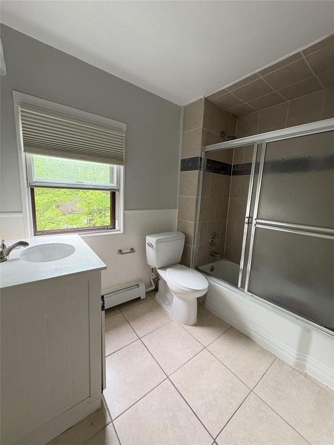 Bathroom with baseboard heating, toilet, enclosed tub / shower combo, tile patterned flooring, and vanity | Image 8