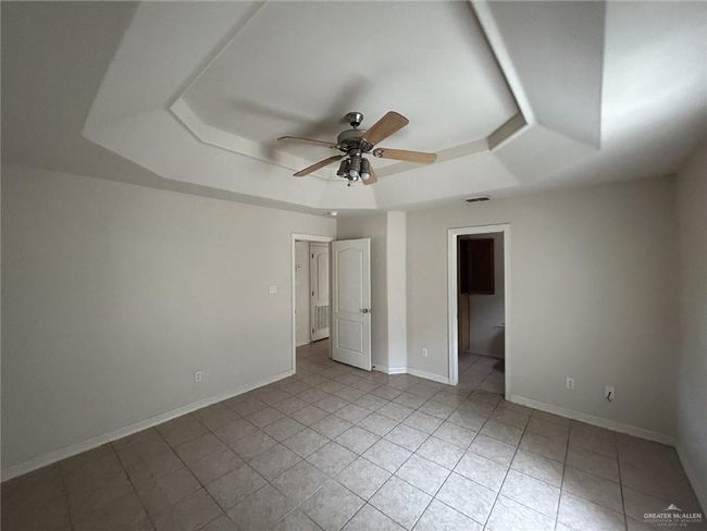 Unfurnished bedroom featuring a raised ceiling, light tile patterned floors, baseboards, ceiling fan, and ensuite bath | Image 10