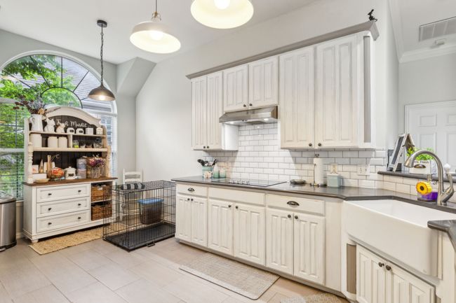 Kitchen with a sink, black electric cooktop, dark countertops, under cabinet range hood, and visible vents | Image 12